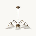 Five-light Clérachic chandelier with white pierced ceramic shades on curved antique brass arms, shown on a plain white background.