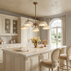 Clérachic chandelier with ceramic shades above a marble-topped kitchen island, with an arched glazed door and cream cabinets behind.
