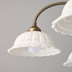 Close view of one white ceramic shade with a pierced leaf pattern and scalloped edge on this Clérachic chandelier, a bulb glowing inside.