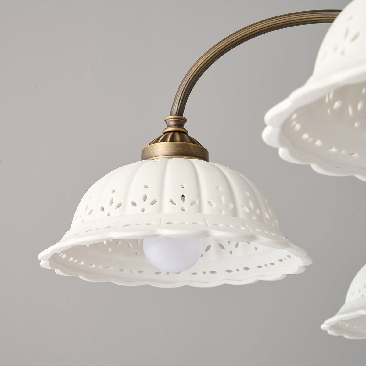 Close view of one white ceramic shade with a pierced leaf pattern and scalloped edge on this Clérachic chandelier, a bulb glowing inside.