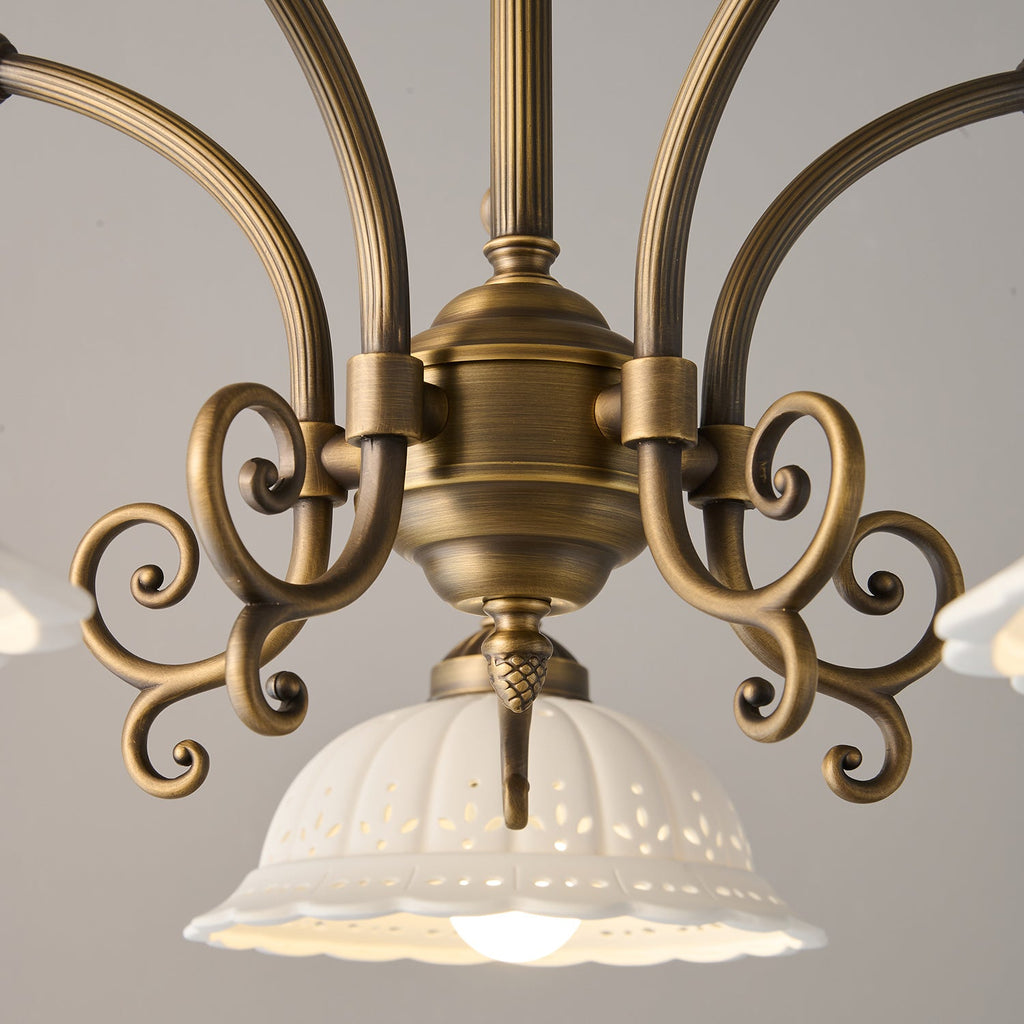 Close view of the scrolled antique brass centre and fluted arms of this Clérachic chandelier, with a ceramic shade below.