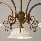 Close view of the scrolled antique brass centre and fluted arms of this Clérachic chandelier, with a ceramic shade below.