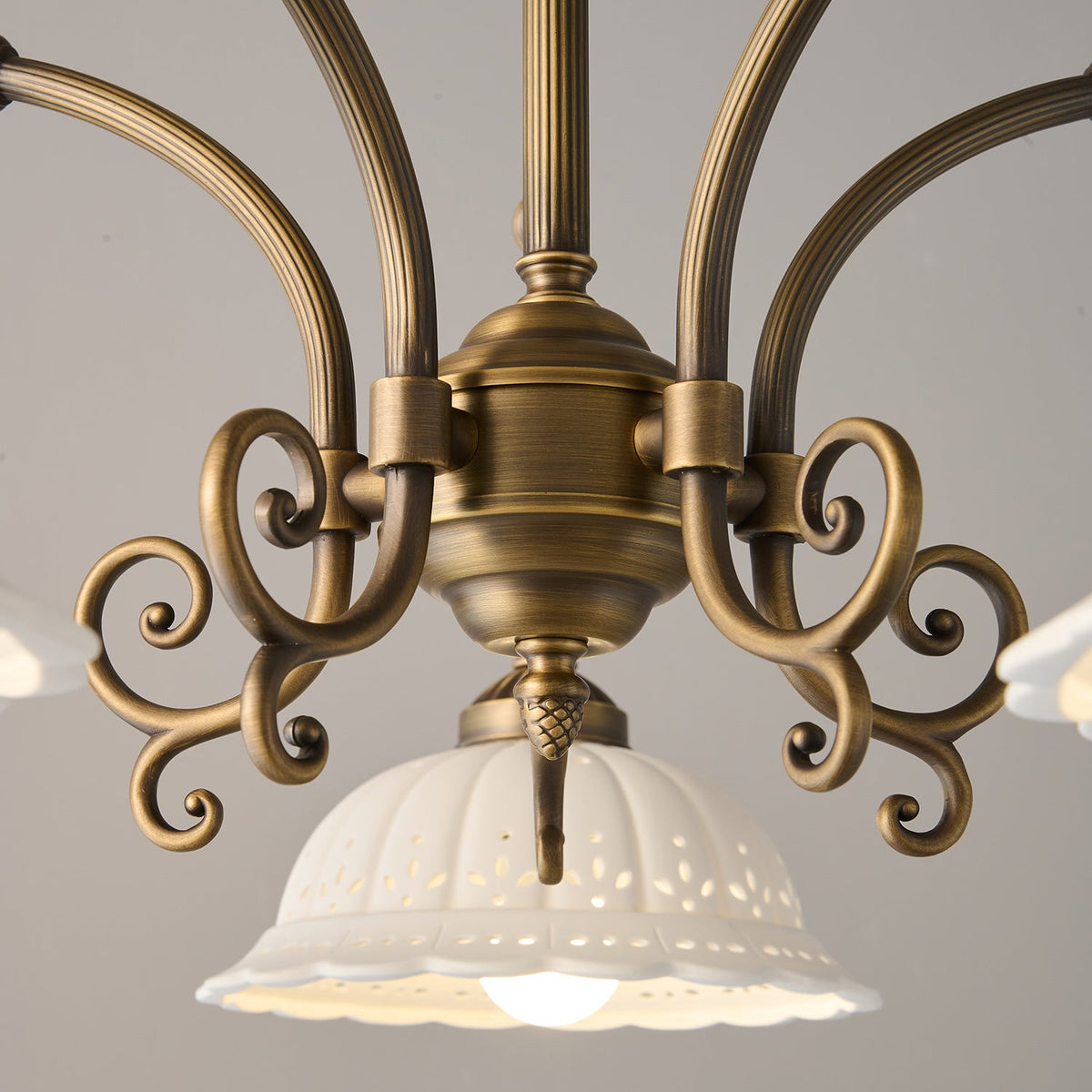 Close view of the scrolled antique brass centre and fluted arms of this Clérachic chandelier, with a ceramic shade below.