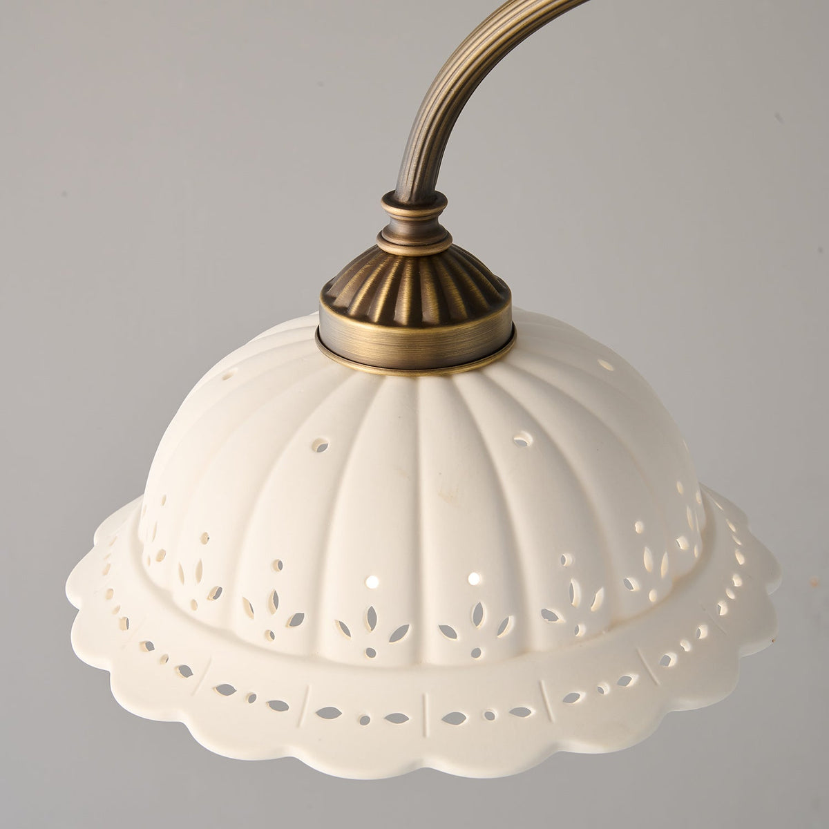 Close view of a ribbed white ceramic shade with pierced edge detail and a brass cap on this Clérachic chandelier.