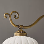 Close view of a brass scroll, a fluted arm and the top of a ceramic shade on this Clérachic chandelier.