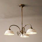Three-light round Clérachic chandelier on a brass rod, its white pierced shades lit and curved arms spreading below a taupe ceiling.