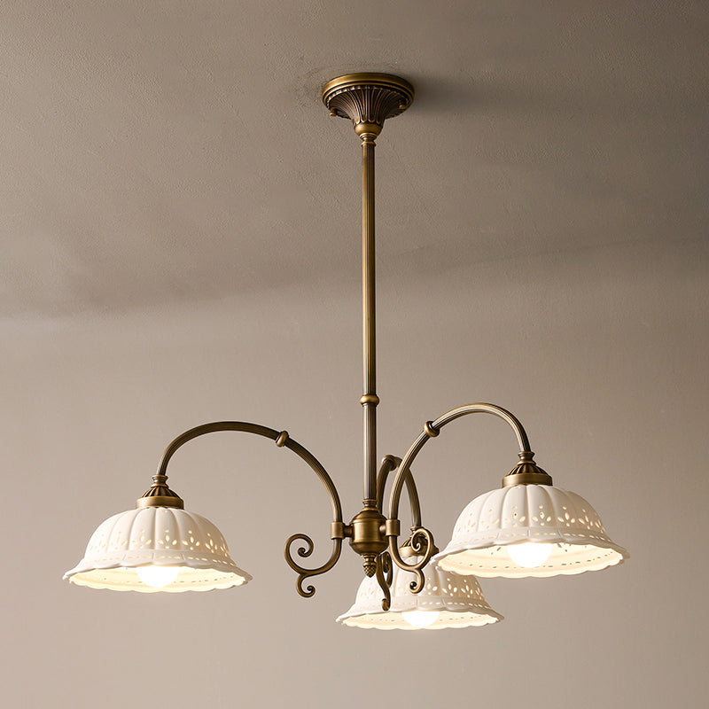 Three-light round Clérachic chandelier on a brass rod, its white pierced shades lit and curved arms spreading below a taupe ceiling.