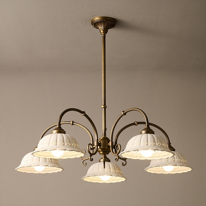 Lit Clérachic five-light chandelier on a long brass rod, hung against a taupe ceiling, with white ceramic shades on curved arms.