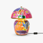 This Clérachic table lamp on a white backdrop, with a hand-painted ceramic base, a dome shade in pink and violet, and a gold rim.