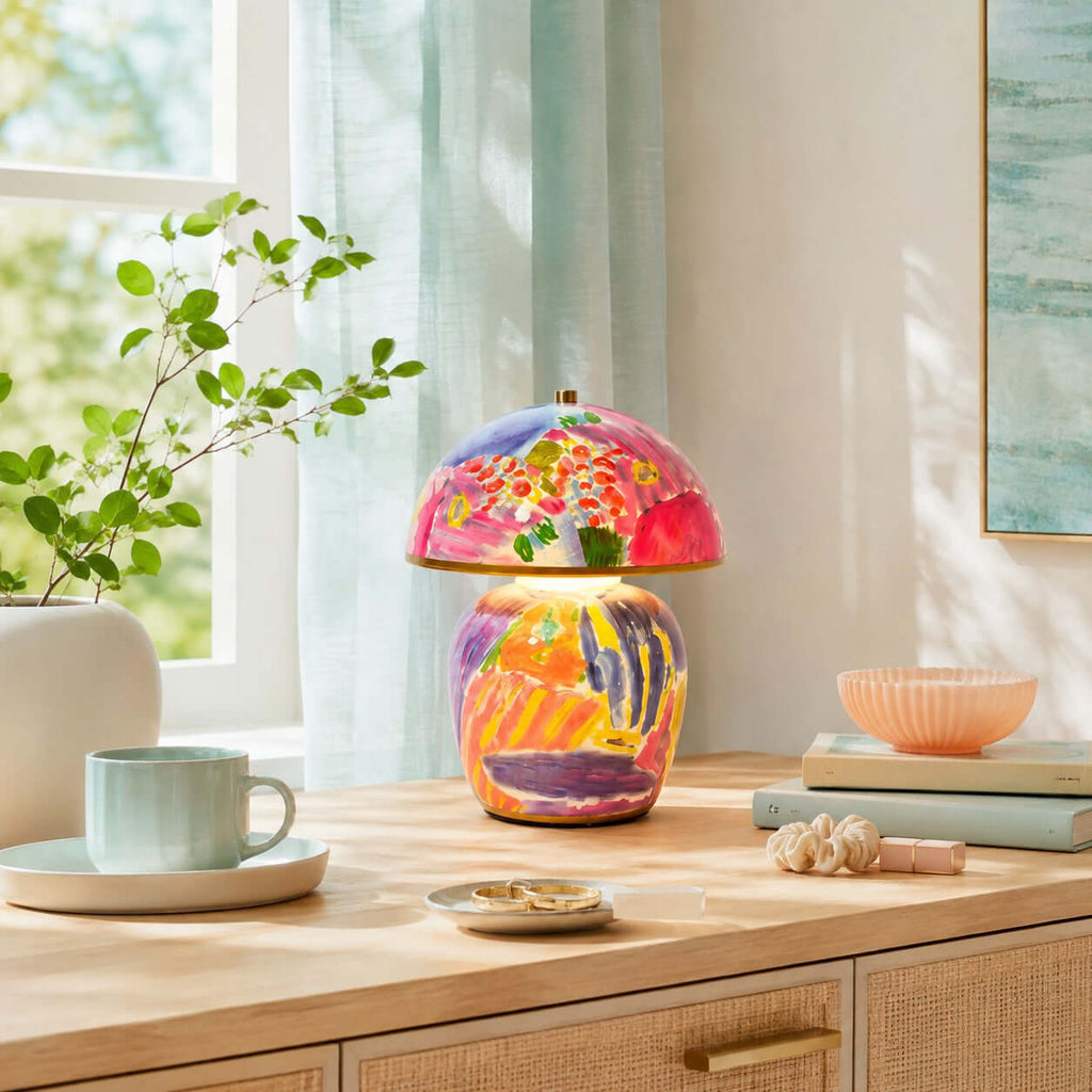 Shown here, a Clérachic table lamp on a light wood sideboard with a pale-blue mug, a peach bowl, shells and a sprig of green in a vase.