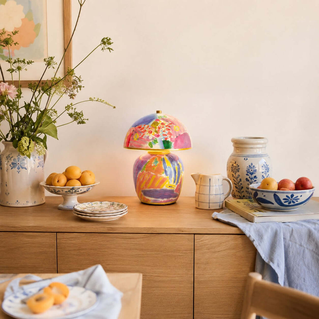 In this photo, a Clérachic table lamp on a wooden sideboard, with a bowl of oranges, blue-and-white china and a vase of wildflowers.