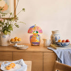 In this photo, a Clérachic table lamp on a wooden sideboard, with a bowl of oranges, blue-and-white china and a vase of wildflowers.