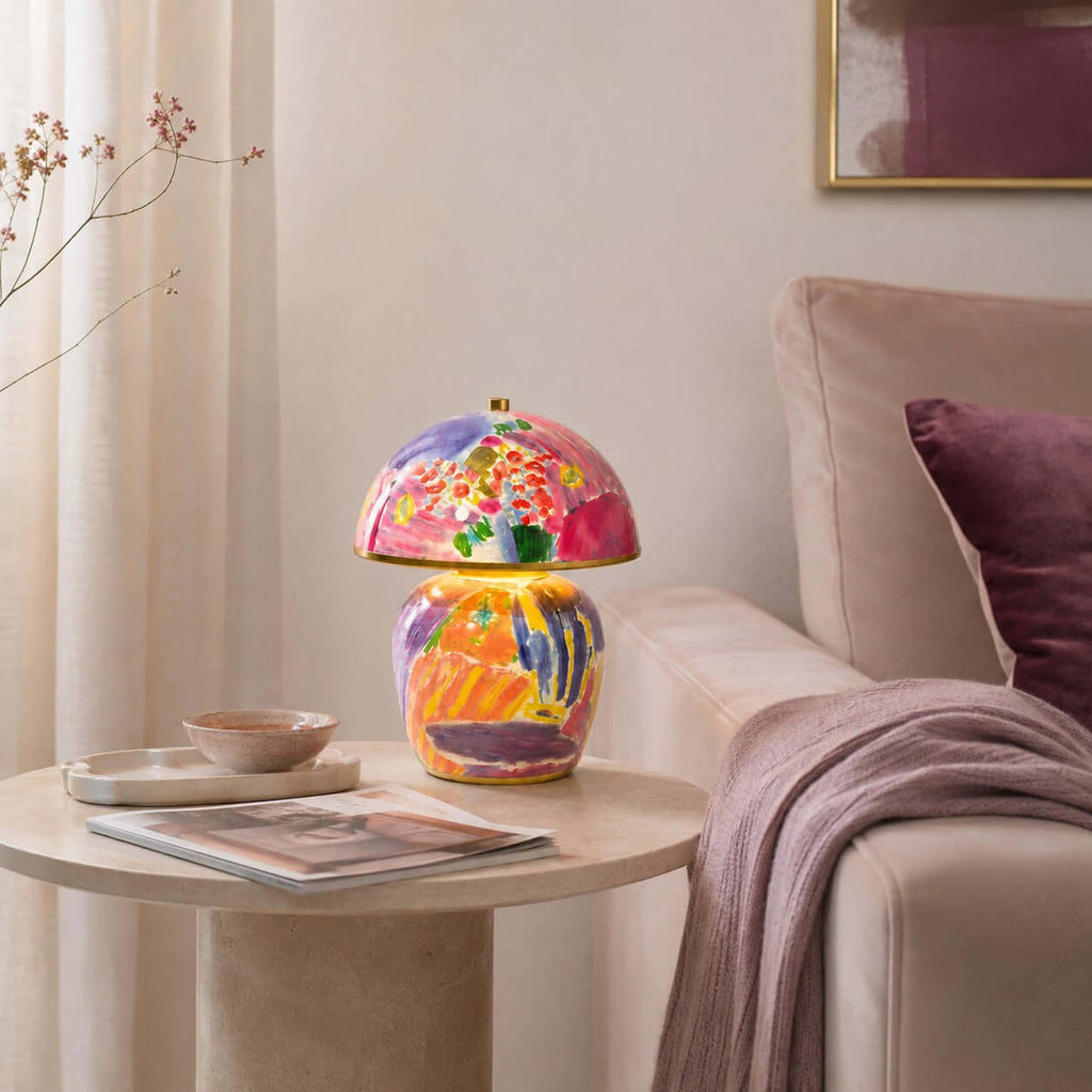 Pictured here, a Clérachic table lamp on a round stone side table next to a pink sofa, with a magazine, a small dish and a plum cushion.