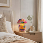 Shown here, a Clérachic table lamp on a pale wooden bedside table, with a cream upholstered headboard, a ribbed vase and a small mug.