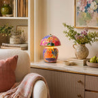 A Clérachic table lamp on a marble-topped cabinet, with a stoneware jug of wildflowers, a pear in a bowl and a framed floral print.