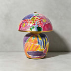 Close, front-on view of this Clérachic table lamp on a grey backdrop, showing the brushstrokes in pink, violet and orange on its ceramic base.