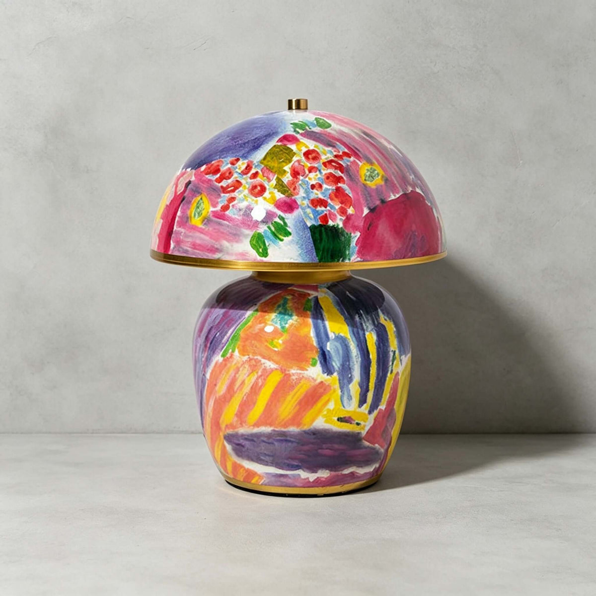 Close, front-on view of this Clérachic table lamp on a grey backdrop, showing the brushstrokes in pink, violet and orange on its ceramic base.