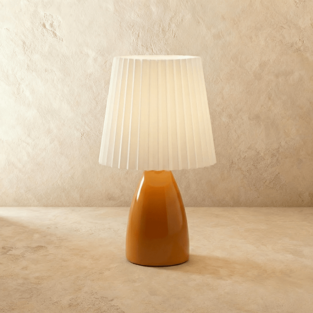 The Clérachic ceramic table lamp in a warm orange finish, paired with a pleated white fabric shade, unlit.