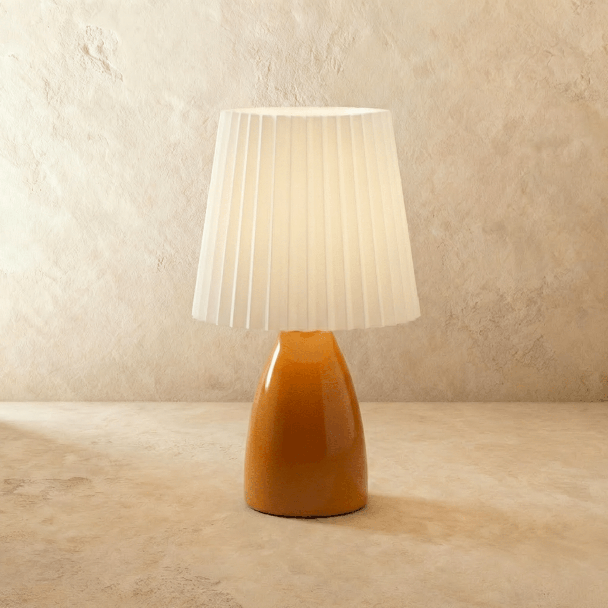 The Clérachic ceramic table lamp in a warm orange finish, paired with a pleated white fabric shade, unlit.