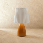 A second angle of the Clérachic orange ceramic table lamp, its pleated white fabric shade shown unlit.
