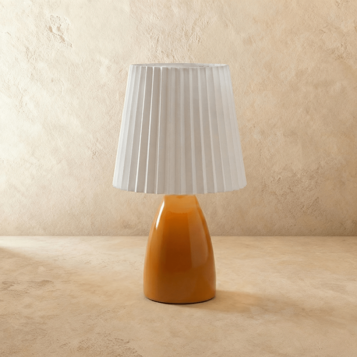 A second angle of the Clérachic orange ceramic table lamp, its pleated white fabric shade shown unlit.