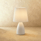 The Clérachic ceramic table lamp in white, its pleated fabric shade glowing warm white on a plain backdrop.