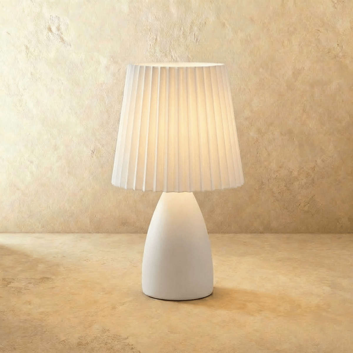 The Clérachic ceramic table lamp in white, its pleated fabric shade glowing warm white on a plain backdrop.