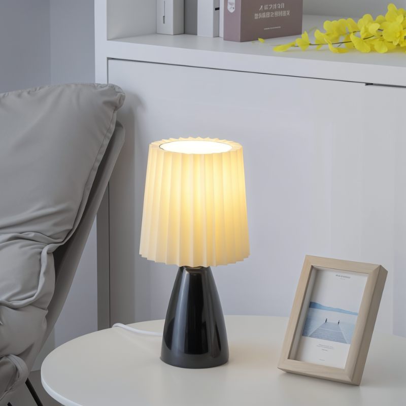 The Clérachic black ceramic table lamp lit on a round table, beside a framed pier photo and shelved boxes.