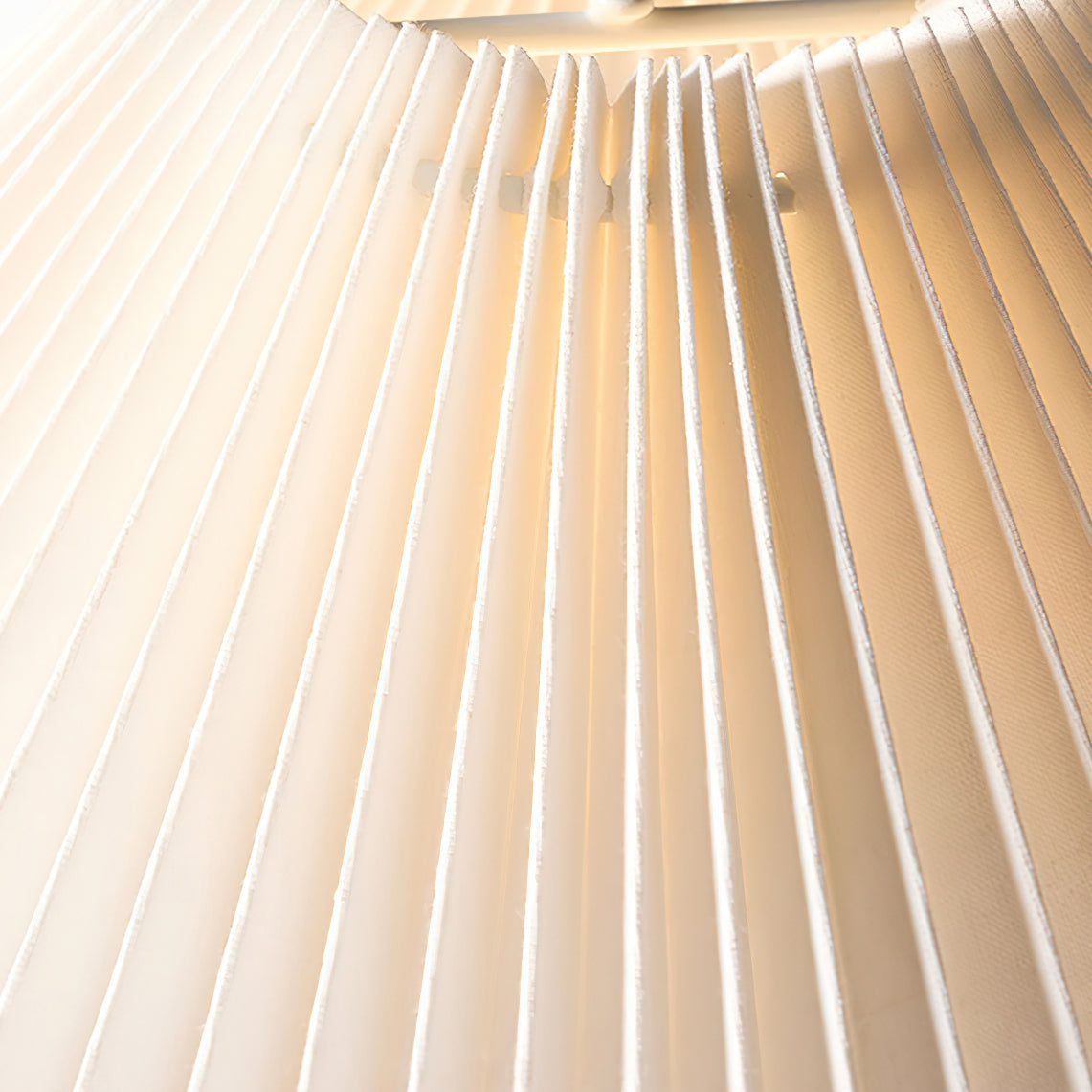 Close view of the fine pleats of this Clérachic lamp shade, lit from inside with a warm glow.