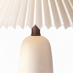Close view of the beige ceramic base of this Clérachic table lamp, with its speckled finish and dark neck under the pleated shade.