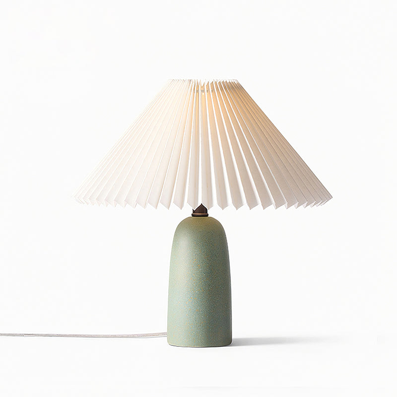 A short green Clérachic table lamp with a lit pleated shade, glowing softly on a plain white backdrop.