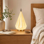Glowing faceted cone lamp from Clérachic on an oak bedside table, beside a pair of glasses, a book and a cream pillow.