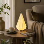 Faceted ceramic lamp from Clérachic on a round wooden side table, beside a cup and saucer and a magazine, next to a grey armchair.