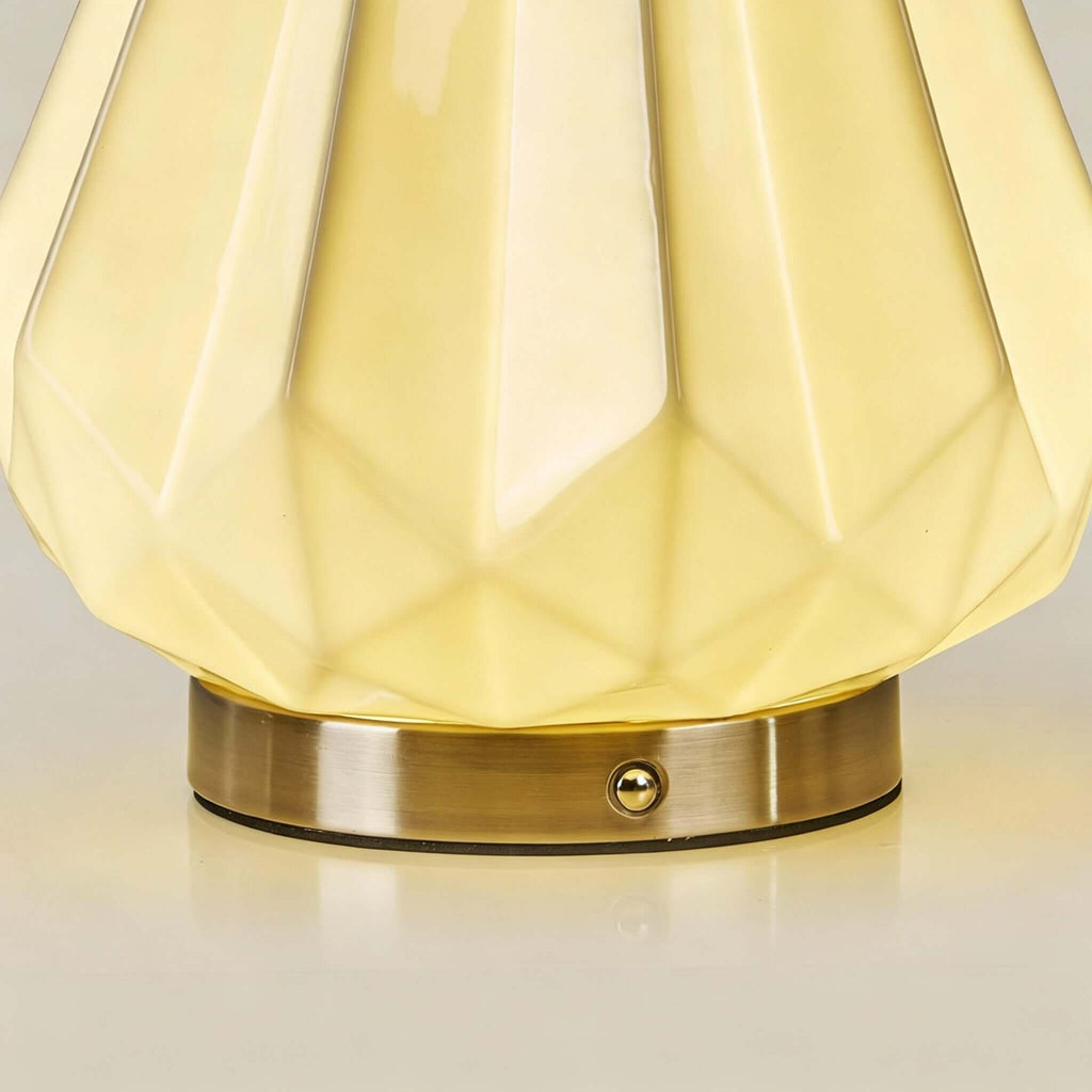 Close view of the glowing faceted ceramic shade and the round brass base with its small touch button, on this Clérachic lamp.