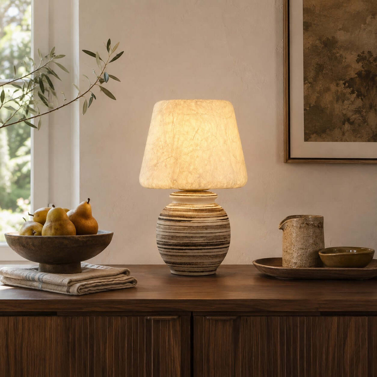 On a dark wood sideboard beside a bowl of pears, this Clérachic table lamp glows warm from its pale shade.