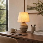 On a wooden desk with a mug, a notebook and a pot of pencils, this Clérachic table lamp lights a corner with a framed landscape behind it.