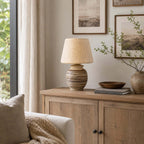 Unlit on a pale oak sideboard, this Clérachic table lamp shows its cream shade next to a wooden bowl and a stack of books.