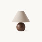 Table lamp from Clérachic with a conical linen shade on a round walnut wood-grain ceramic base, shown on a white backdrop.