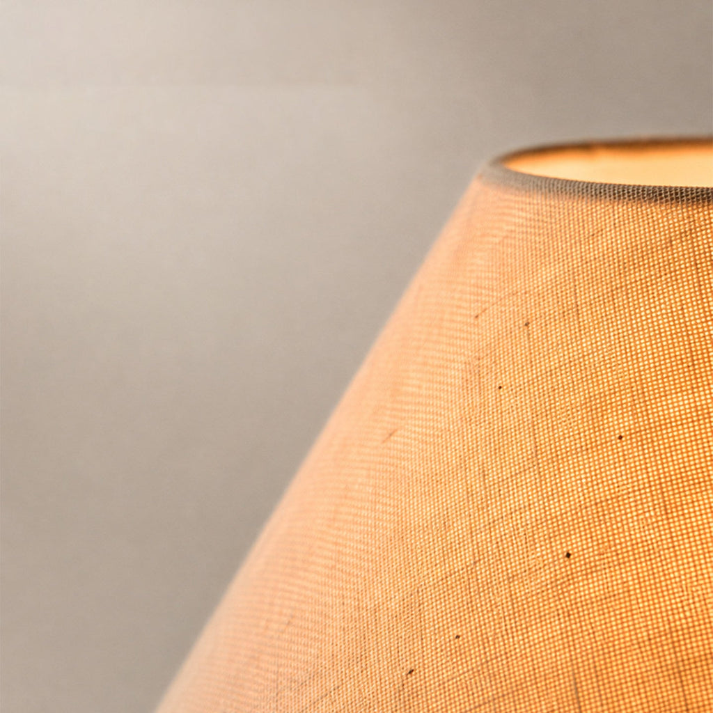 Close view of the lit linen weave on the conical shade of this Clérachic table lamp, glowing warm at its opening.