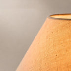 Close view of the lit linen weave on the conical shade of this Clérachic table lamp, glowing warm at its opening.