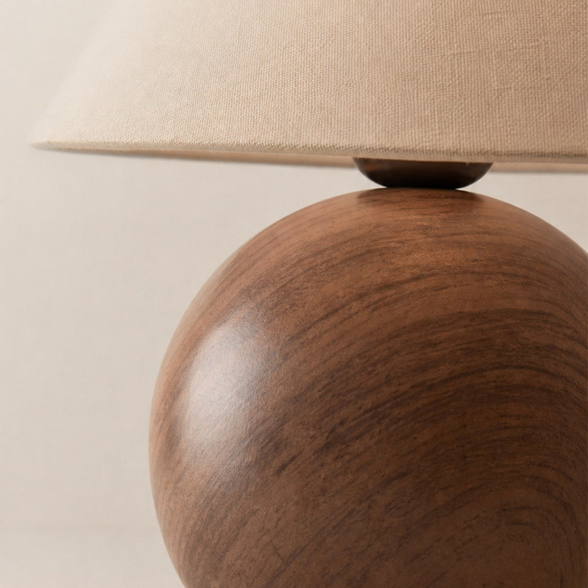 Close view of the glossy walnut wood-grain ceramic ball base of this Clérachic table lamp, with the linen shade above it.