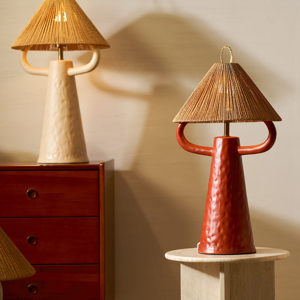 This Clérachic table lamp in terracotta stands on a round stone table, a cream version above it on a dark red cabinet.