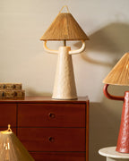Cream ceramic Clérachic table lamp with curved arms and a rope shade on a walnut cabinet, with a stack of books to the left.