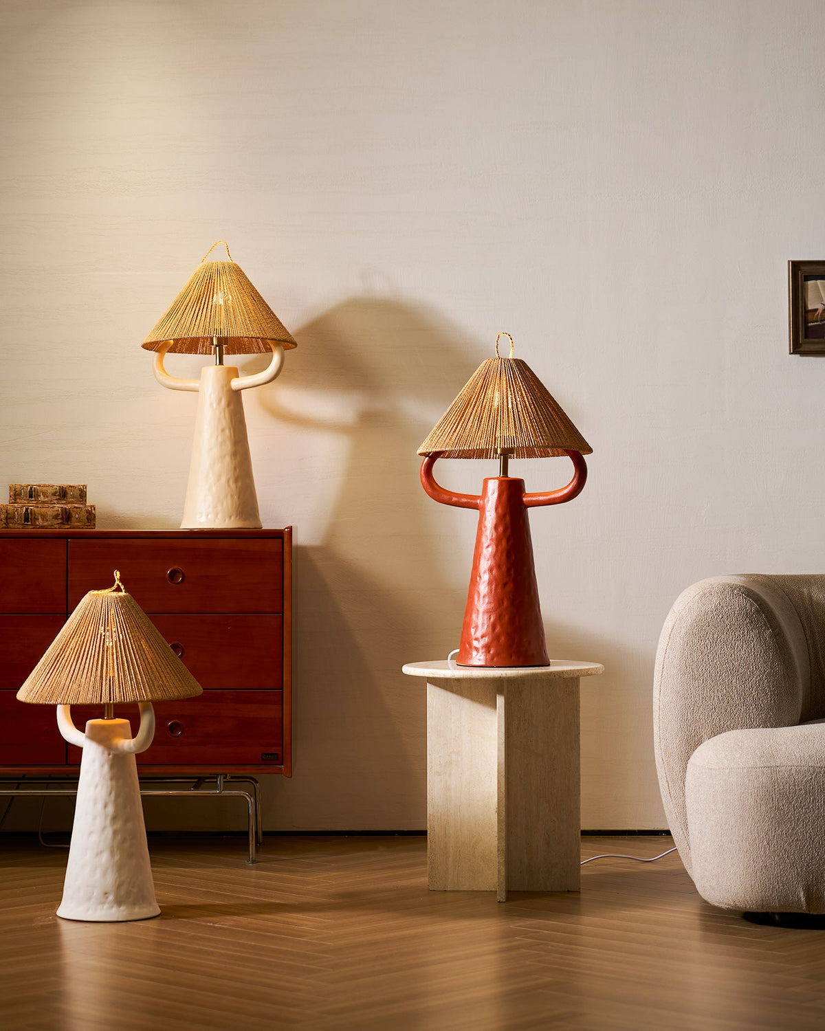Wider view of three Clérachic table lamps in cream, terracotta and white around a walnut cabinet, a stone plinth and a boucle chair.