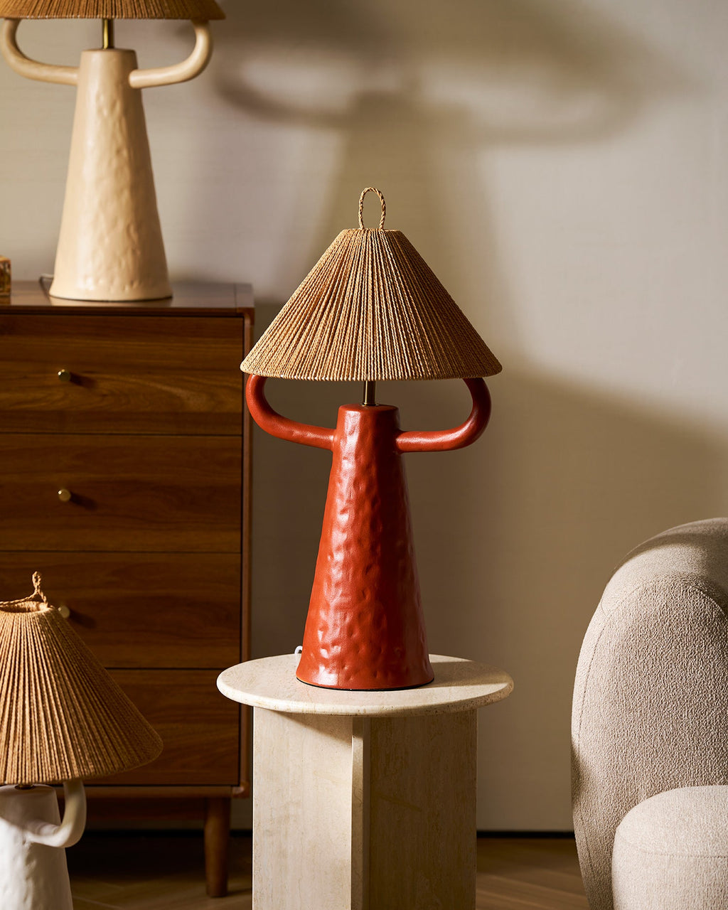 Terracotta Clérachic lamp on a round stone table in front of a walnut chest, with a cream lamp above and a white one below.