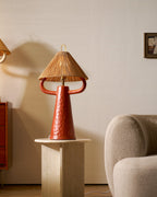 A terracotta ceramic lamp with a rope shade stands on a stone side table beside a cream boucle armchair; from Clérachic.