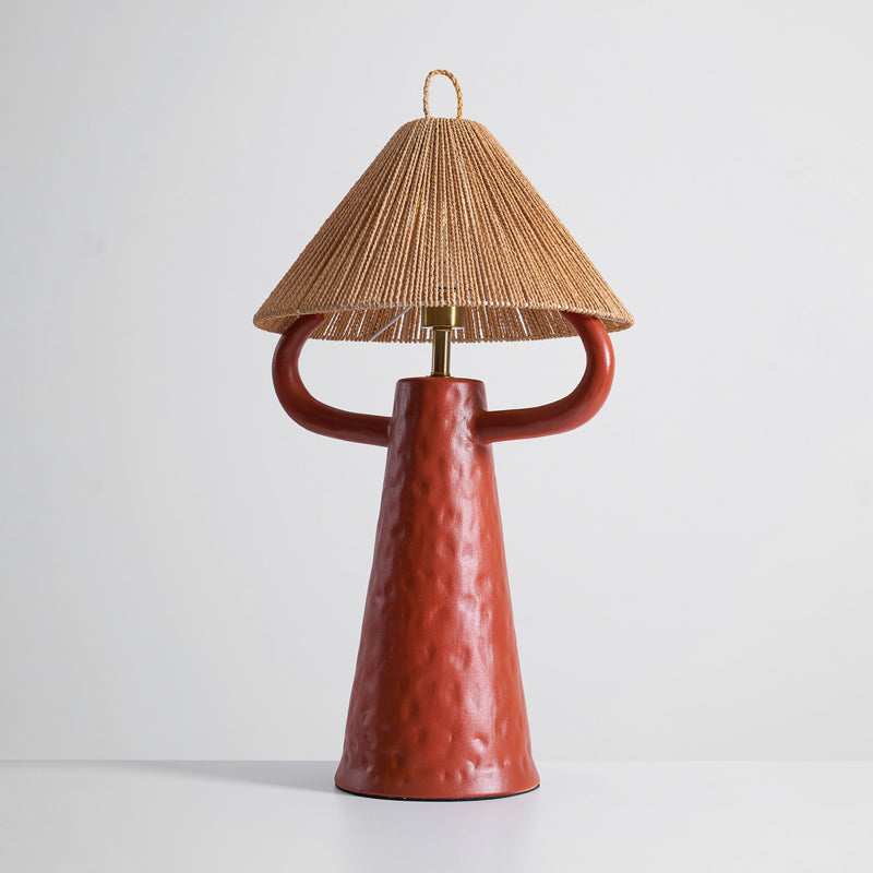 Terracotta Clérachic table lamp on a pale grey surface, with a textured ceramic base, rounded arms and a woven shade.