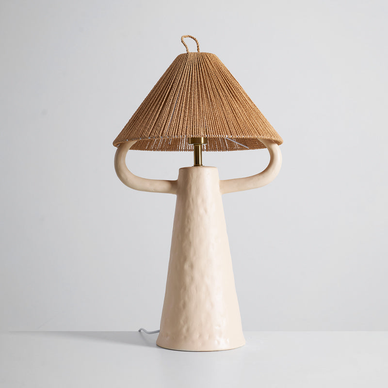 Cream ceramic table lamp with an arm on each side and a cone shade of twisted rope, on a pale surface; this Clérachic lamp.