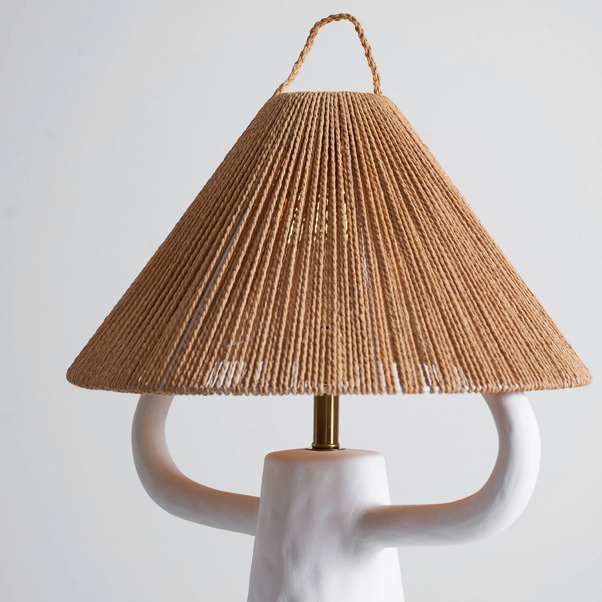 Rope shade of this Clérachic table lamp seen from slightly below, the cone of twisted strands above two white ceramic arms and a brass stem.