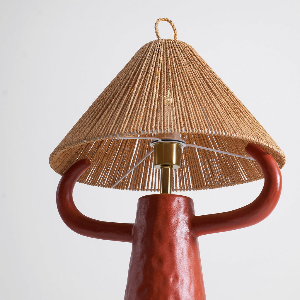 Terracotta arms curve up under the open underside of the rope shade, with the brass stem between them; a Clérachic table lamp.